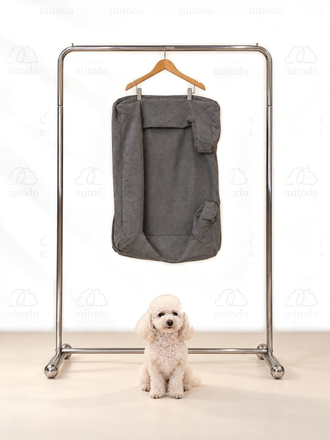 Kumo Bed Extra Cover in Charcoal Gray hanging on a rail, with a white poodle sitting below