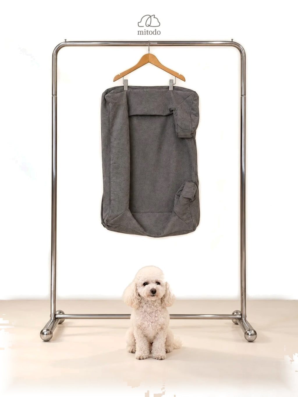 Mitodo Kumo Bed Extra Cover in Charcoal Gray hanging on a rail, with a white poodle sitting below
