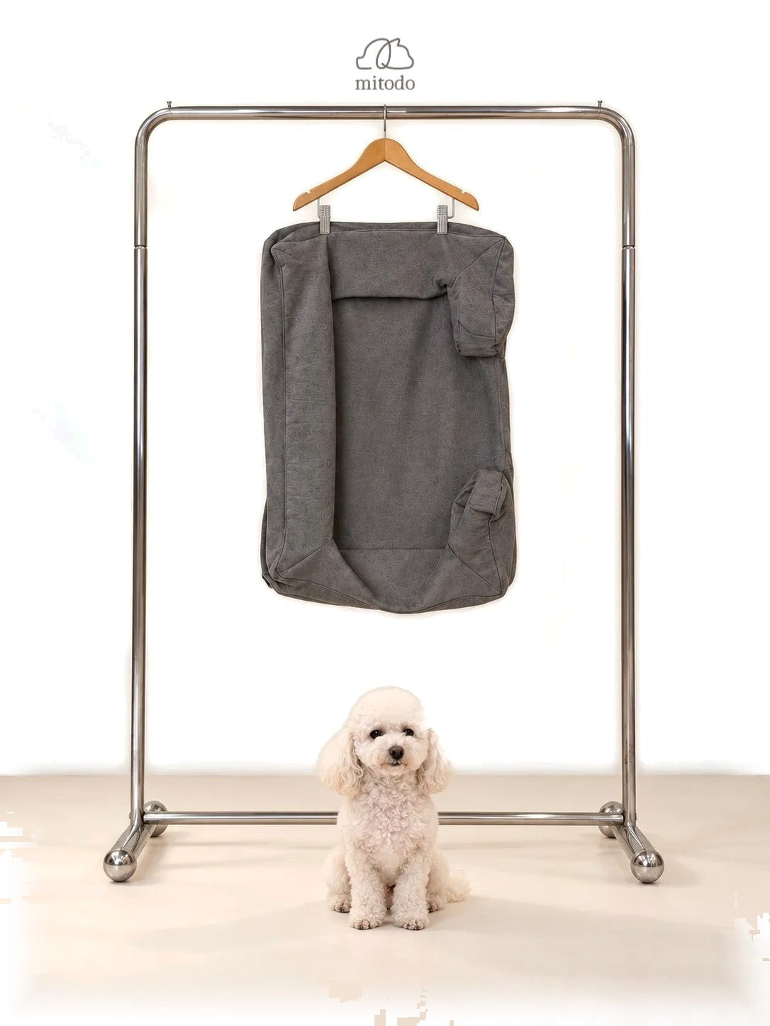 Mitodo Kumo Bed Extra Cover in Charcoal Gray hanging on a rail, with a white poodle sitting below