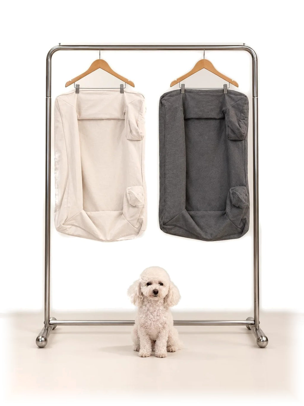 Mitodo Kumo Bed Extra Covers in both colours hanging on a rail, with a white poodle sitting below