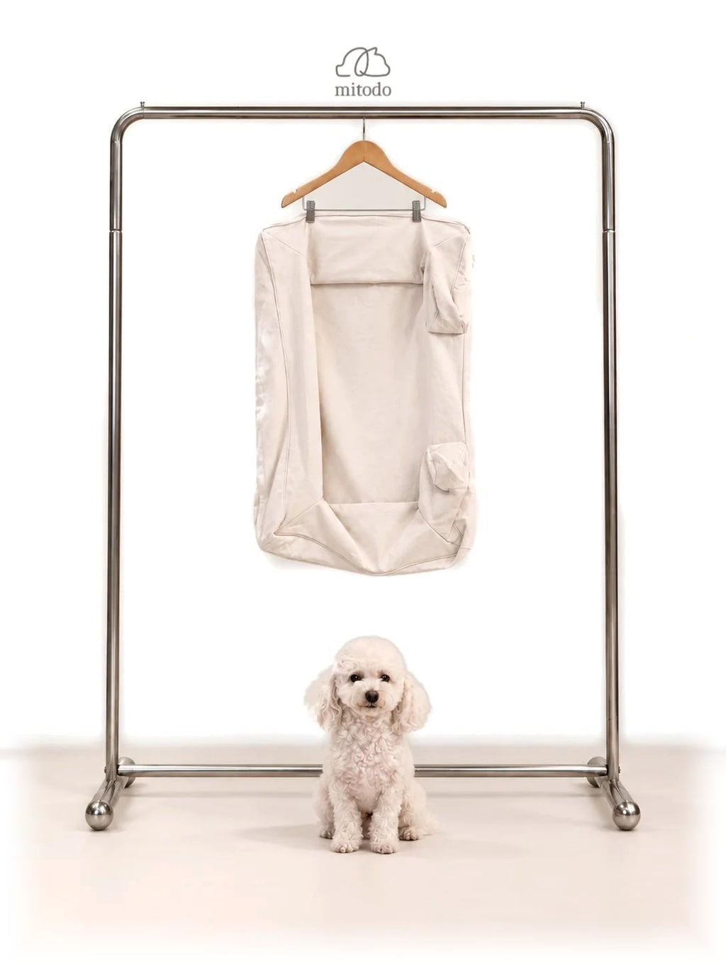 Mitodo Kumo Bed Extra Cover in Cream hanging on a rail, with a white poodle sitting below