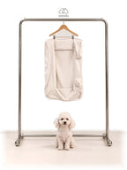 Mitodo Kumo Bed Extra Cover in Cream hanging on a rail, with a white poodle sitting below