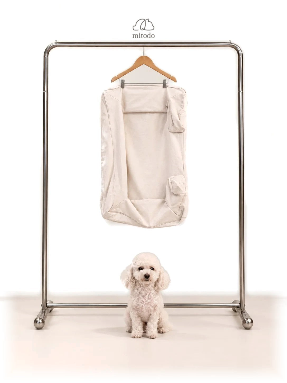 Mitodo Kumo Bed Extra Cover in Cream hanging on a rail, with a white poodle sitting below